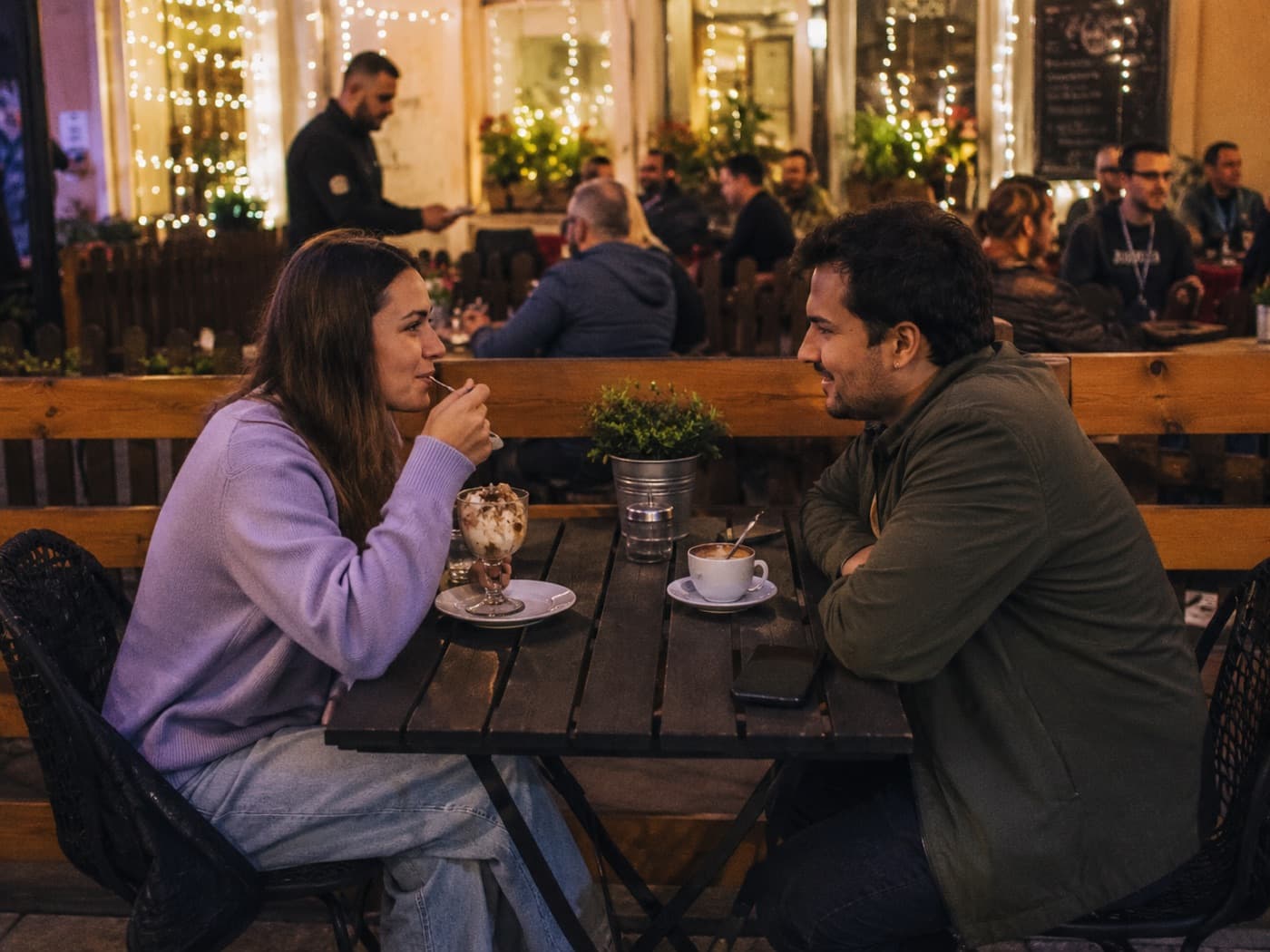 A couple sharing dessert and coffee at an outdoor table strung with lights